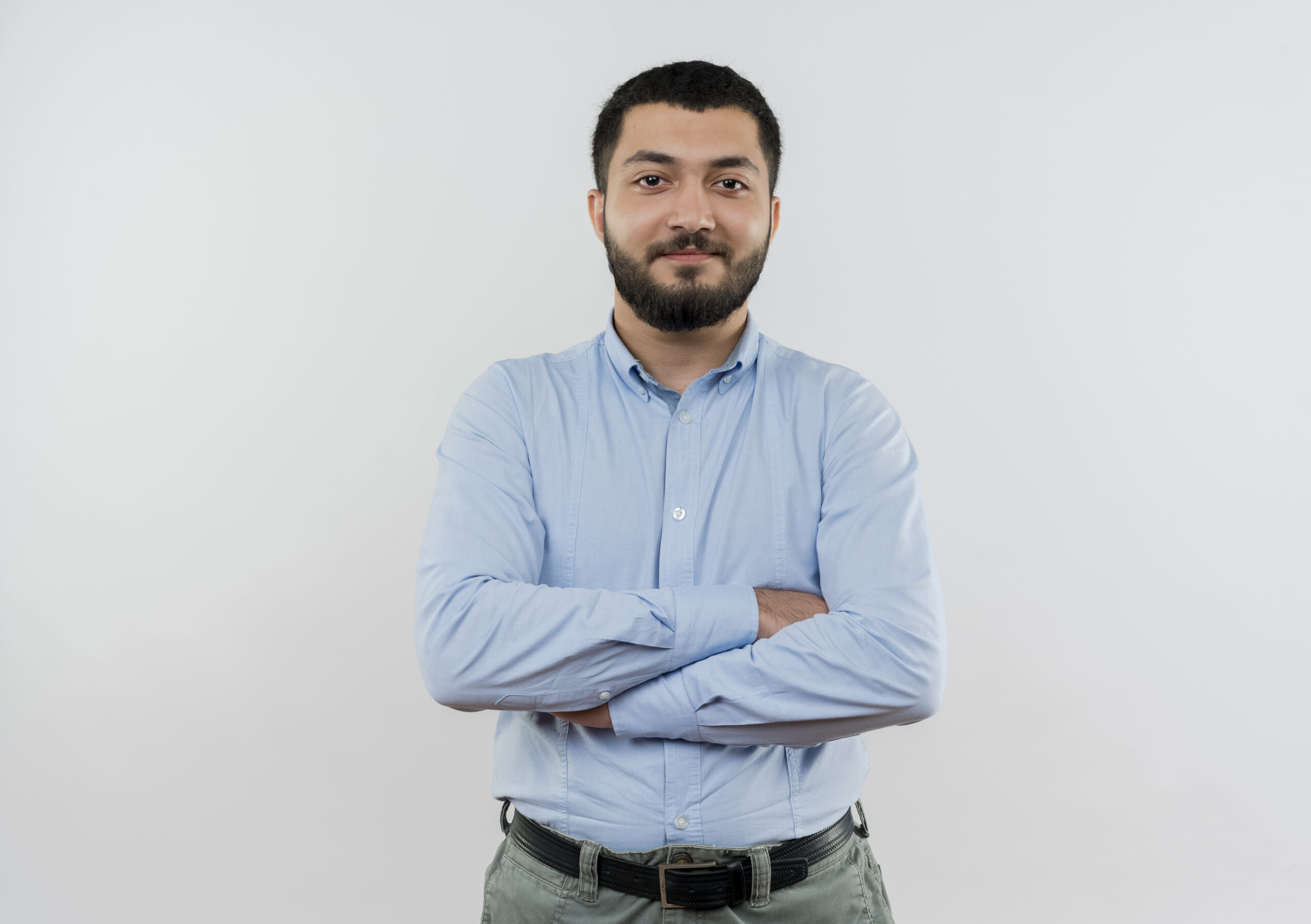 young bearded man in blue shirt looking at camera with crossed arms smiling confident standing over white background